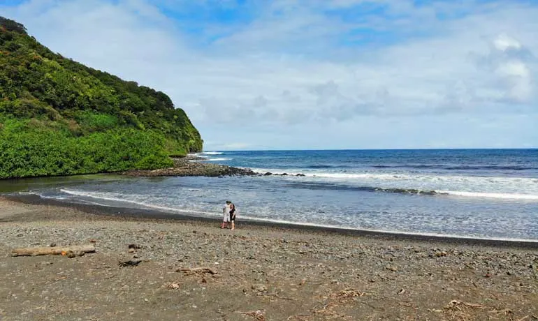 couple on an empty beach on the road to hana with hillside in background