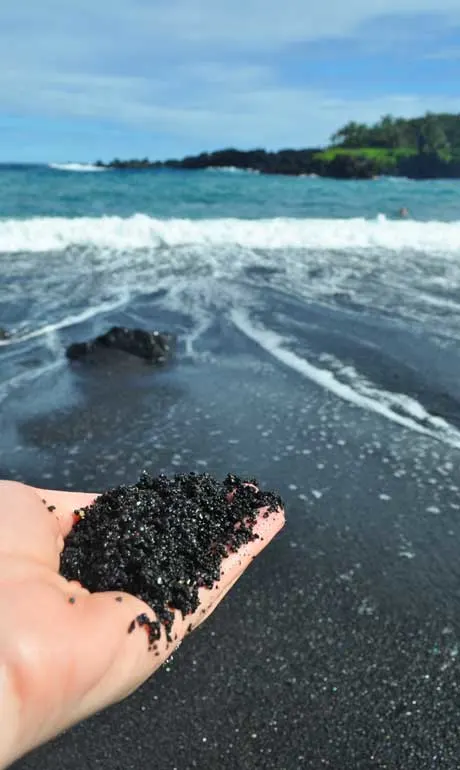 hand holding black sand with beach in background
