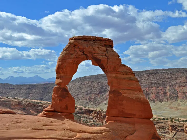 arches national park hikes photo of large orange arch with desert scene behind on partly cloudy day