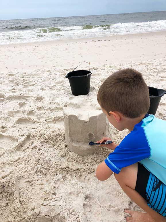 child learning to make a sandcastle with waves in the background