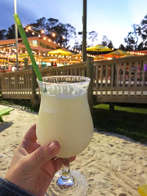 holding a pina colada in the evening with lights in background