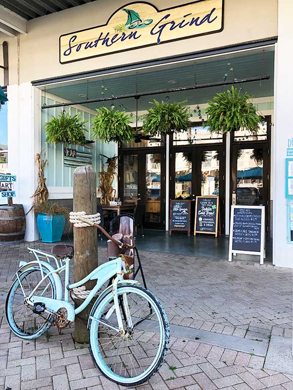 southern grind coffee at the wharf orange beach storefront including antique bike, plants and store signs