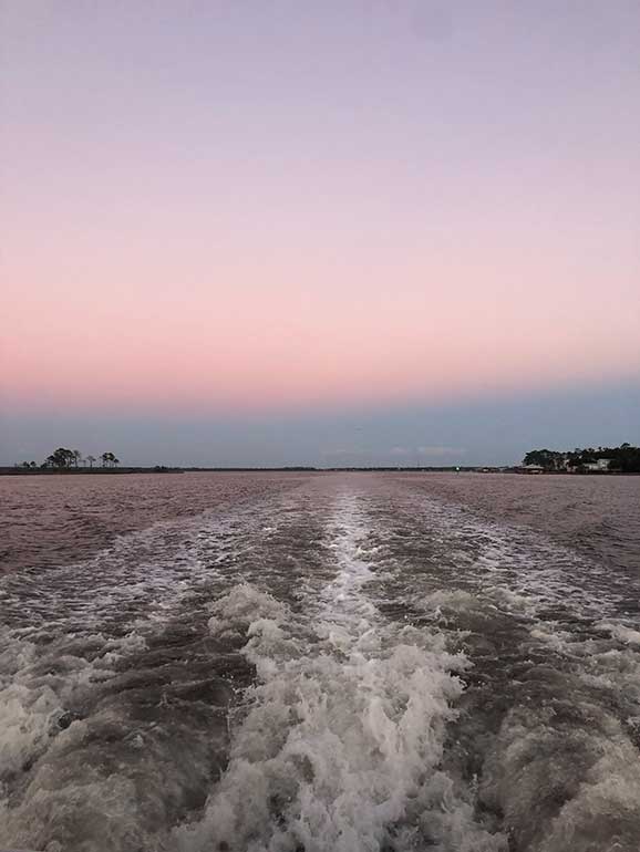 boat ride at sunset with pink sky and boat waves