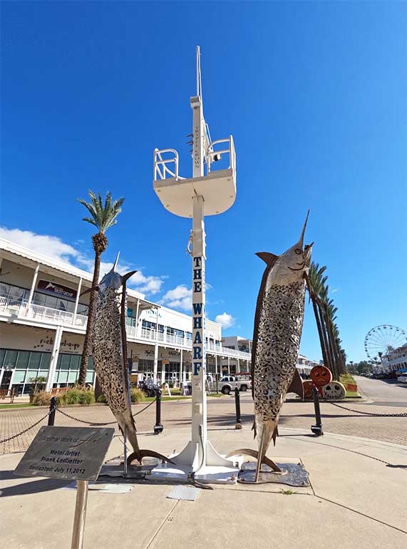wharf in orange beach with large marlin statues, palm trees and buildings in background