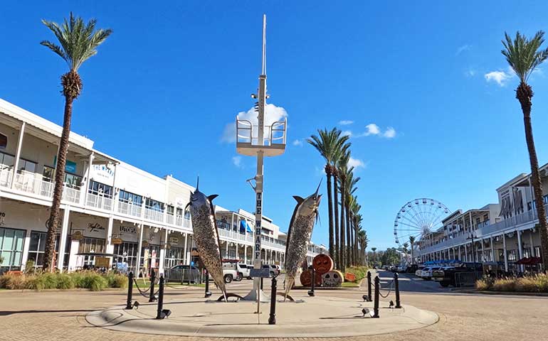 the wharf entrance with sculpture fish, palm trees and shopping center