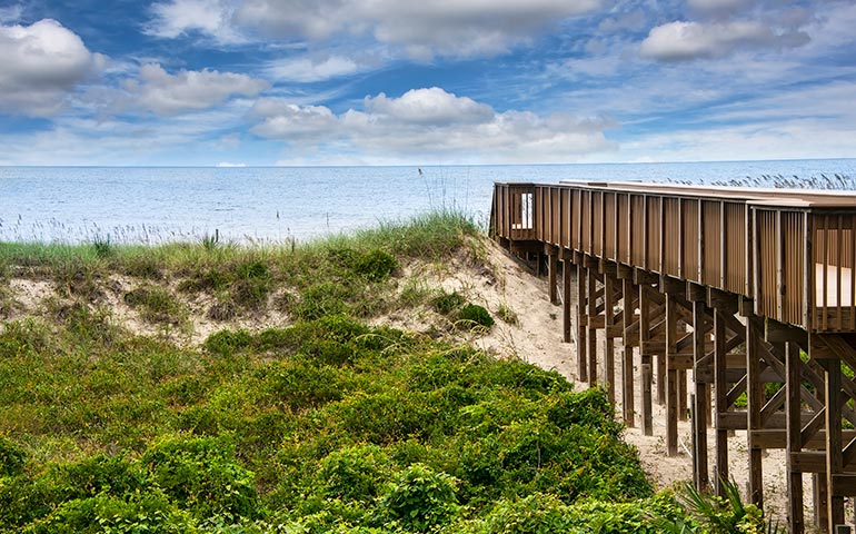 Amelia island pier with green bushes and blue sky with clouds, best kid friendly beaches in Florida