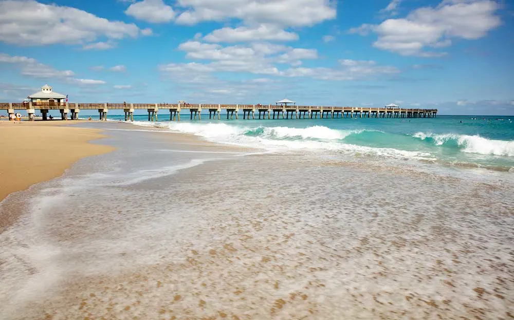 beach pier in background with white waves and yellow sand, one of the best beaches in Florida for families 