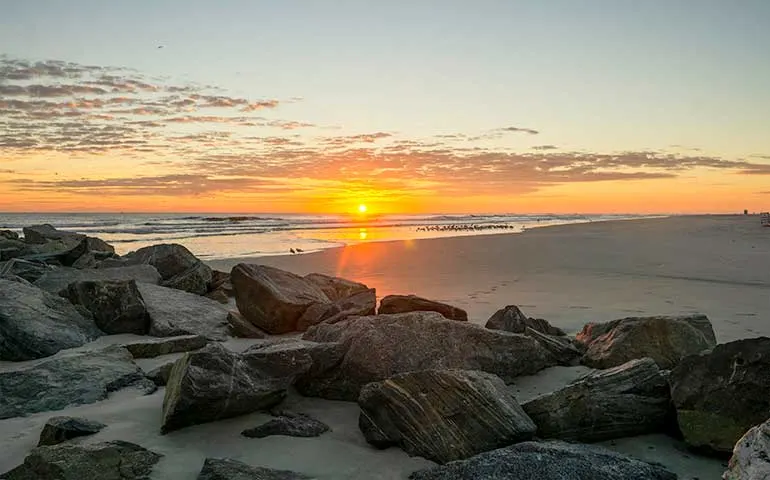 Best beaches in Florida for families: New Smyrna Beach at sunset with rocks in foreground orange sunset in sky
