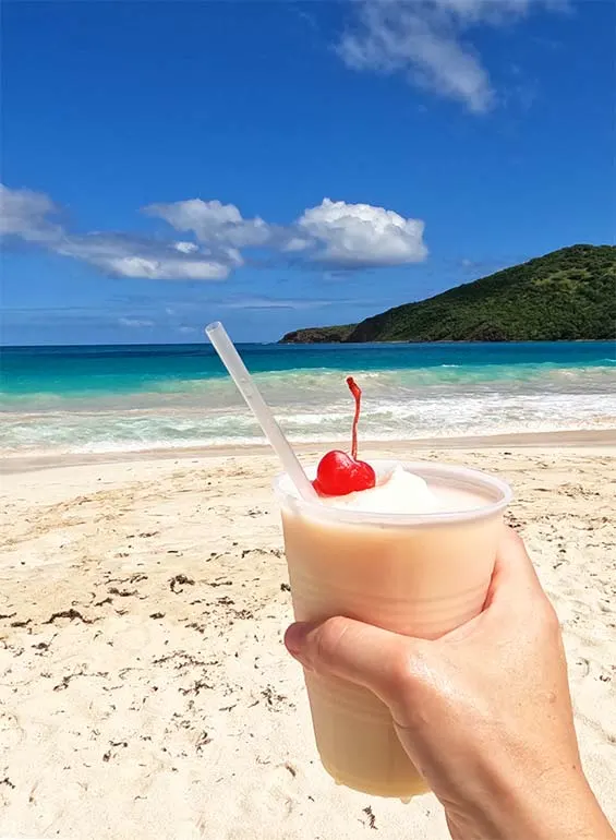 pina colada cup with cherry and beach waves in background