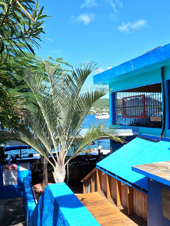 dinghy docks restaurant during the day with blue building and palm tree