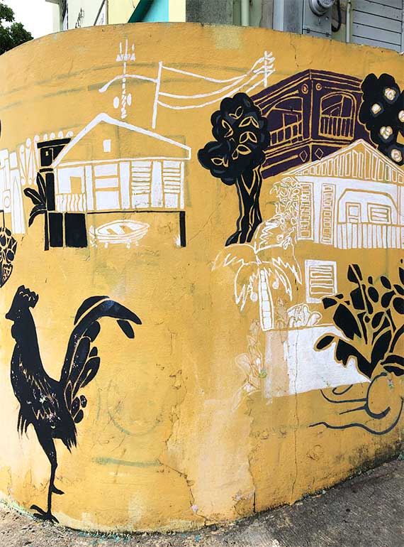 yellow street art with black and white objects - chicken, house, palm tree