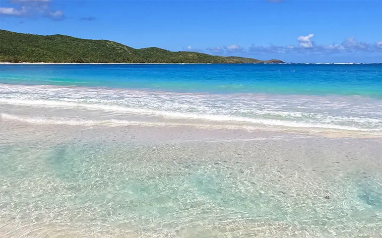 Caribbean Sea light turquoise water with pink sandy bottom and green hills in background