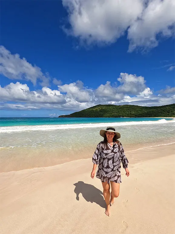 woman walking on beach with waves in background wearing beach cover and hat