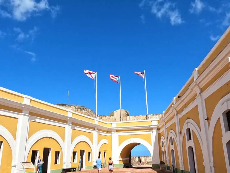 old San Juan things to do visit del Morrow with yellow and white historic building 3 flags flying atop and blue sky