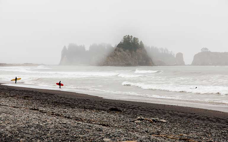 rocky seashore with white waves on a foggy day with two surfers in wet suits