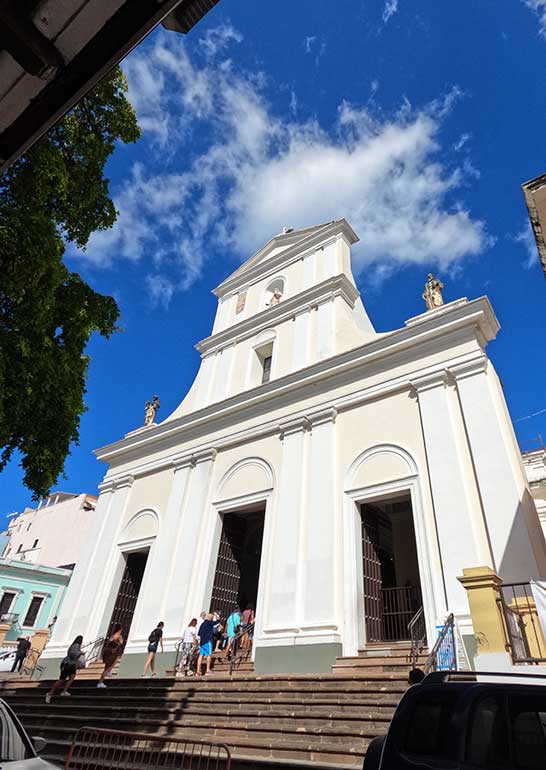 exterior of old cathedral with steps up to tall church with white facade, top things to see in old San Juan