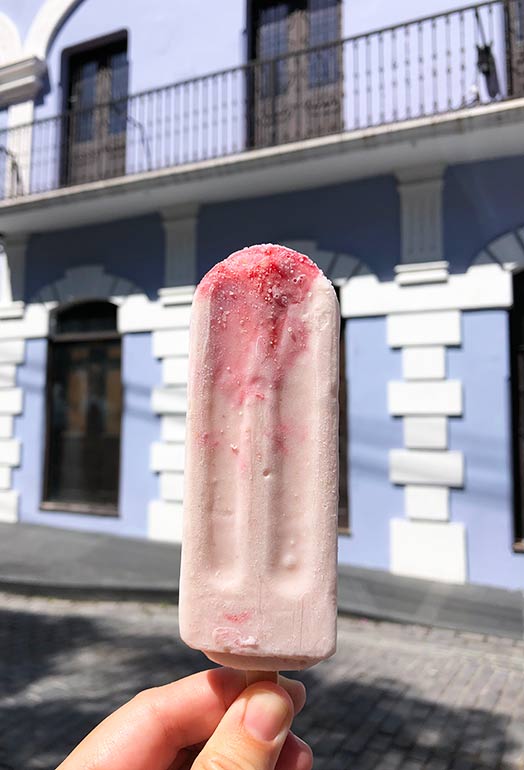 top things to do in old San Juan-eat pink and popsicles against purple building in background