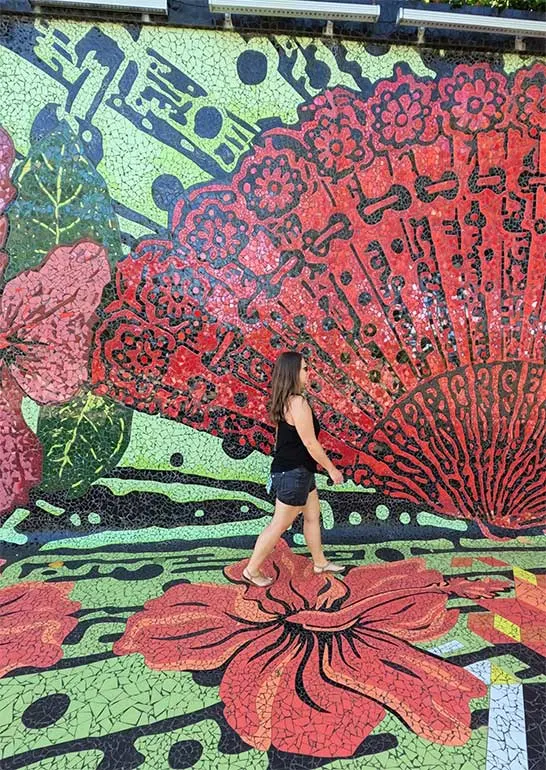 woman walking on mosaic tile mural large red fan, flowers and greenery