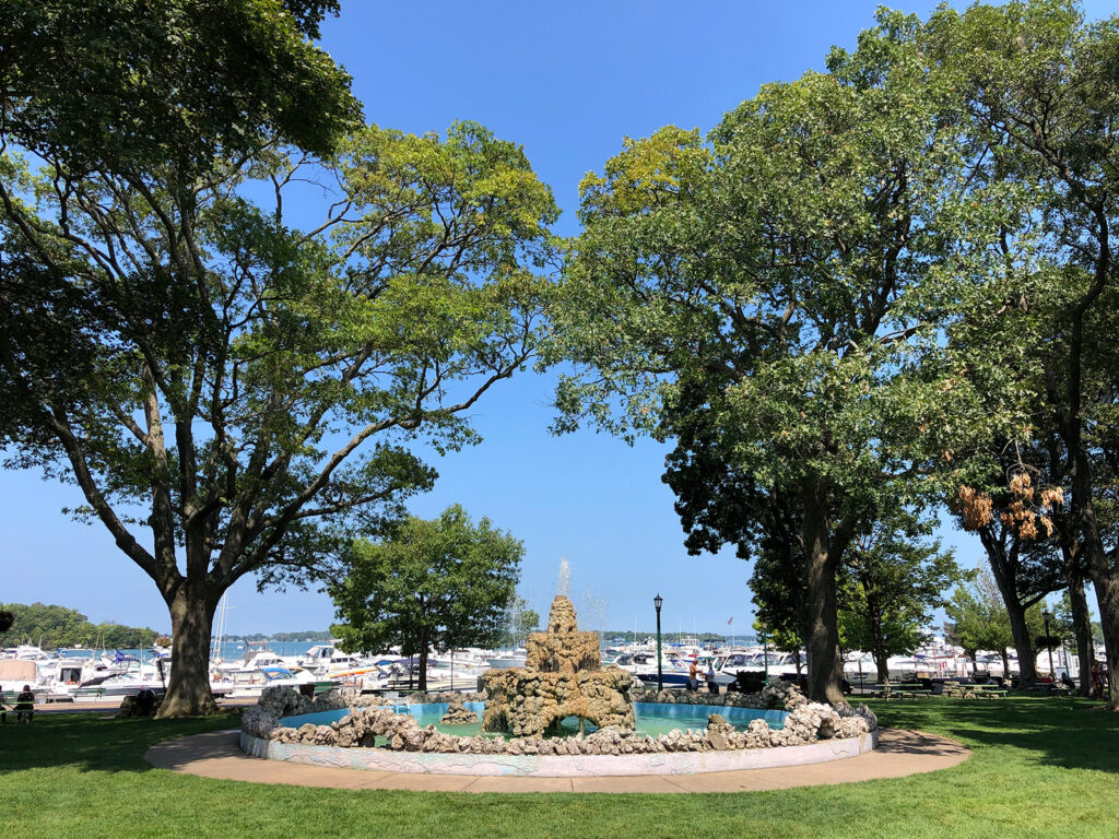 fountain with large trees flowing water and marina in background