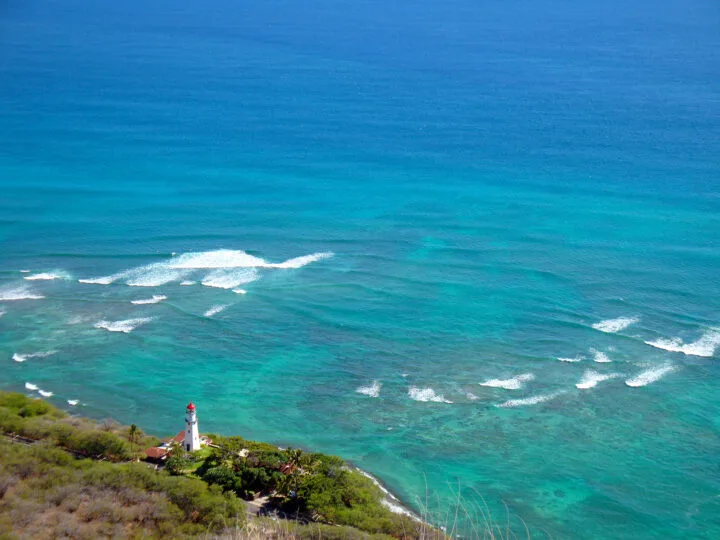 view looking down at teal ocean white waves treelined coast and lighthouse