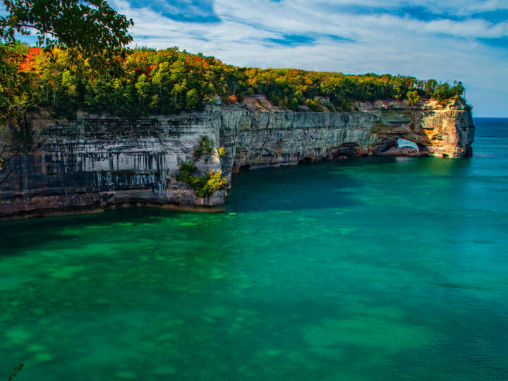 best hiking in the midwest pictured rocks in Michigan with bright water multi colored trees and large cliffs