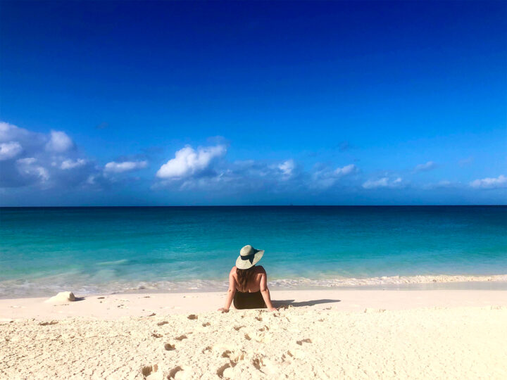 pic of woman sitting on white sand beach with dark blue water