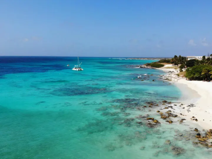 best place to vacation in January pic of white beach, rocky shore and catamaran in distance