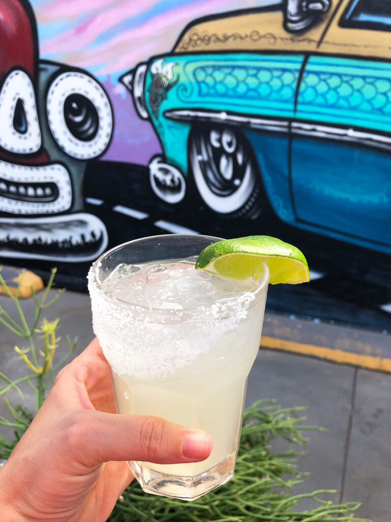 hand holding margarita with colorful mural in background