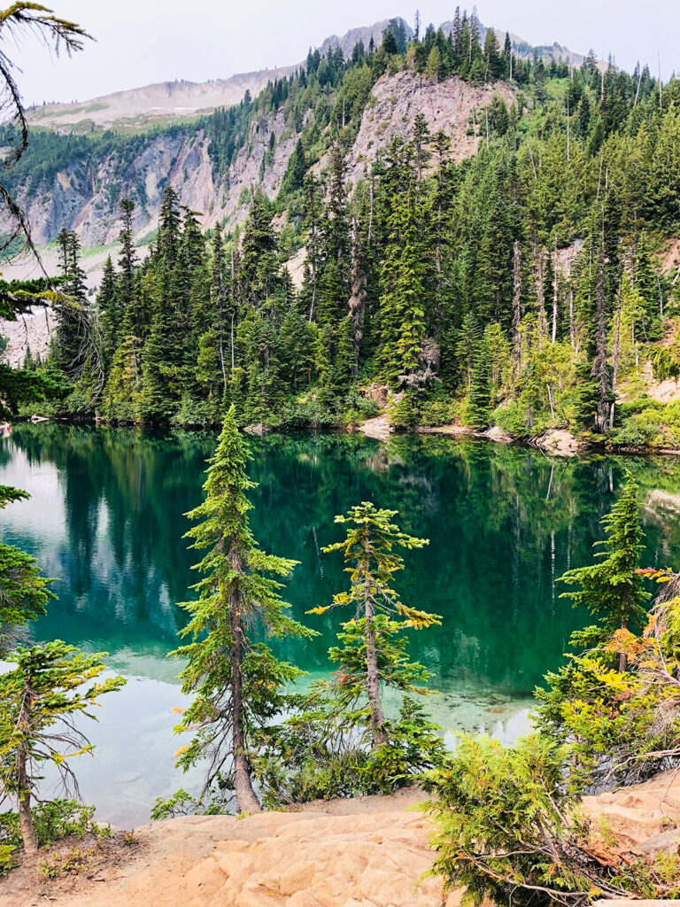 teal colored lake with forest trees and mountain in background