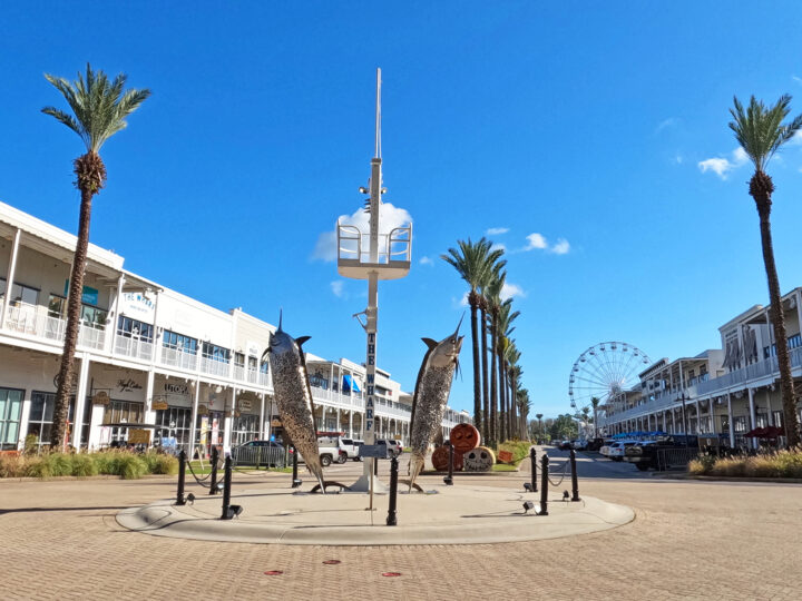 the wharf entrance with sculpture fish, palm trees and shopping center
