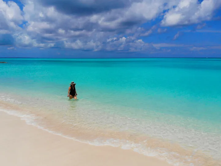 turks and caicos photo of woman walking in ocean bright teal water blue sky and tan sand