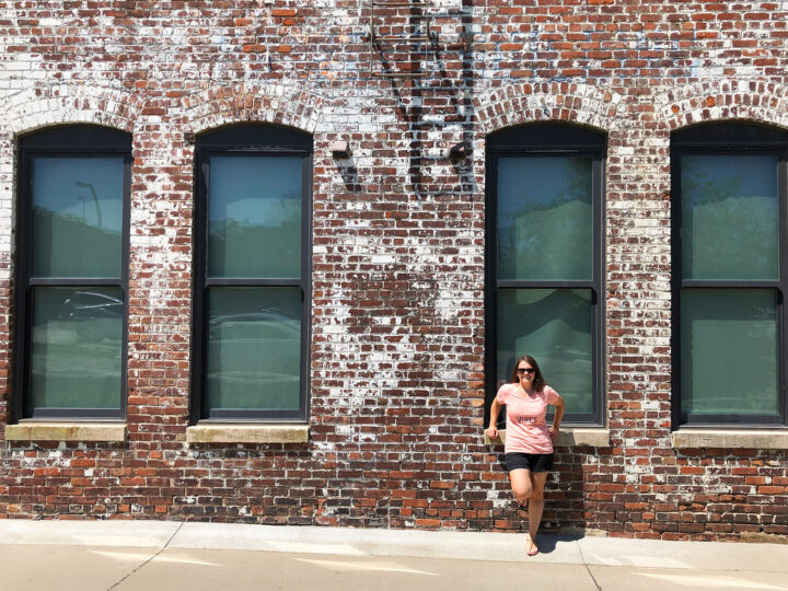 Omaha photo spots woman standing on brick wall with 4 windows wearing peach shirt and shorts