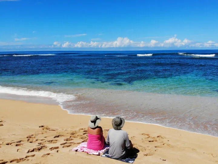 best snorkeling kauai photo of couple sitting on beach with blue water tan sand blue sky