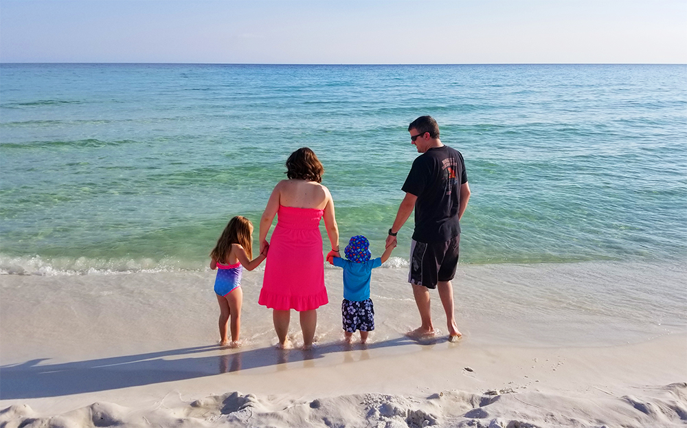 family travel parents and two kids standing on beach with teal water white sand