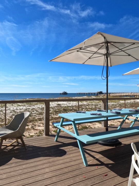 blue table with umbrella on deck facing ocean - orange beach restaurants on the water