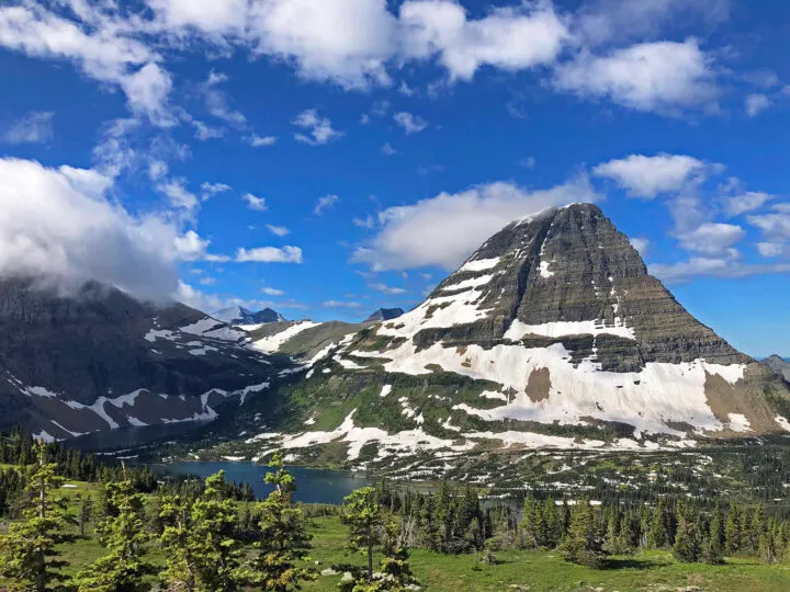 glacier national park hikes picture of mountain peak with snow and lake with low hanging clouds and forest