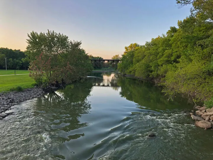 estherville Iowa river with trees and bridge in distance at sunset