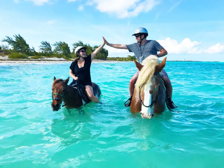 horseback riding turks and caicos couple on two horses in teal water on sunny day