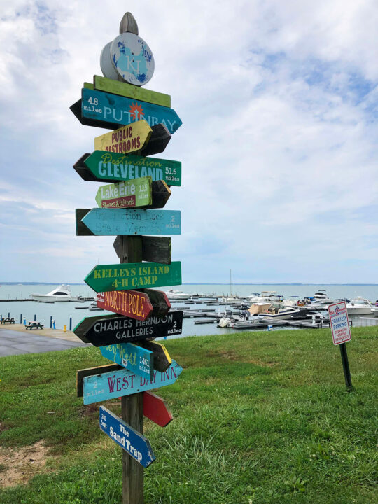 sign on Kelleys island ohio with lots of arrows and activities with marina in background