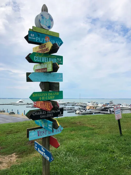 sign on Kelleys island ohio with lots of arrows and activities with marina in background