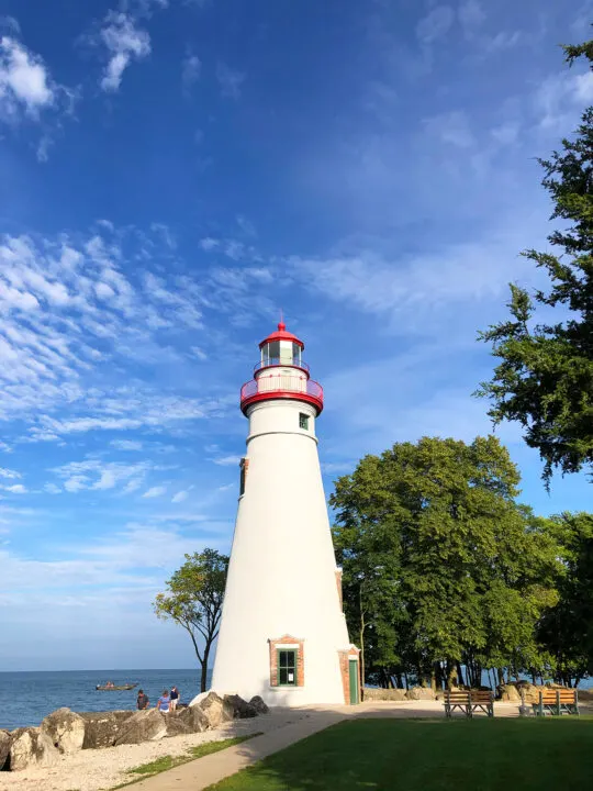 white and red lighthouse with blue sky trees along shoreline