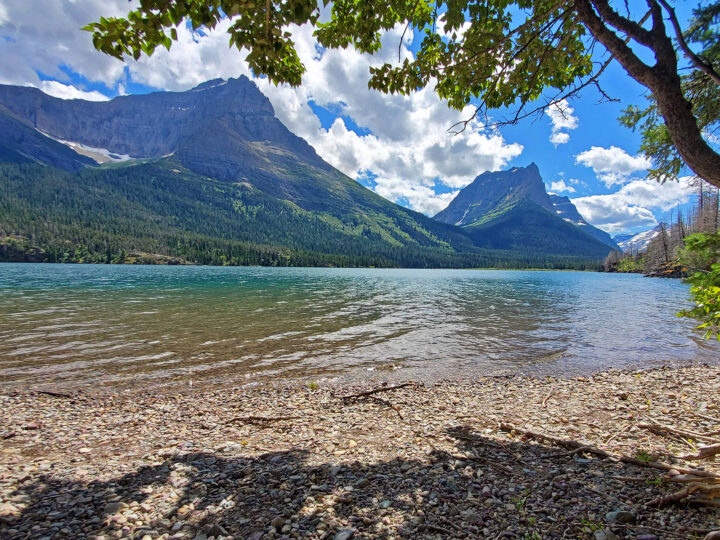 national parks to visit in summer sitting on beach under tree with mountains and lake