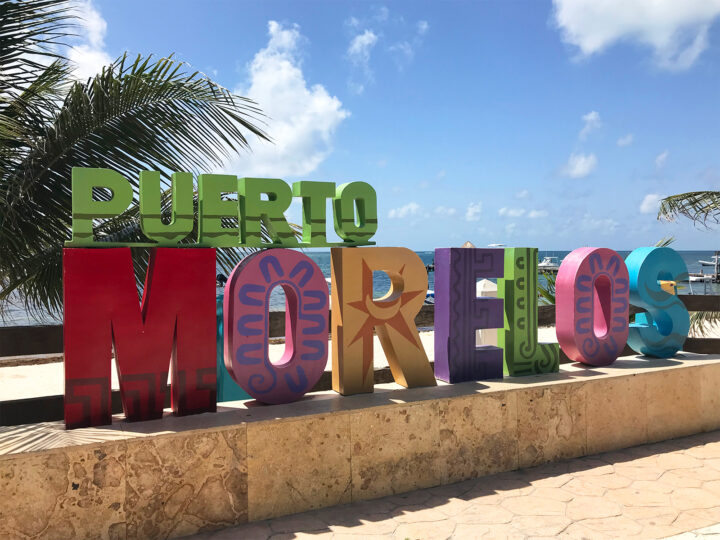Puerto Morelos Mexico sign large colorful letters with palm trees and ocean in background