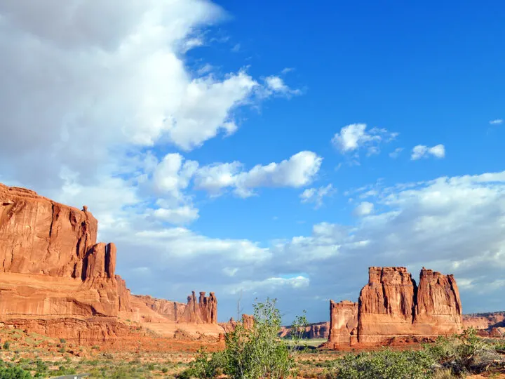 things to do in moab view of jagged red rock cliffs in desert scene with blue sky and clouds