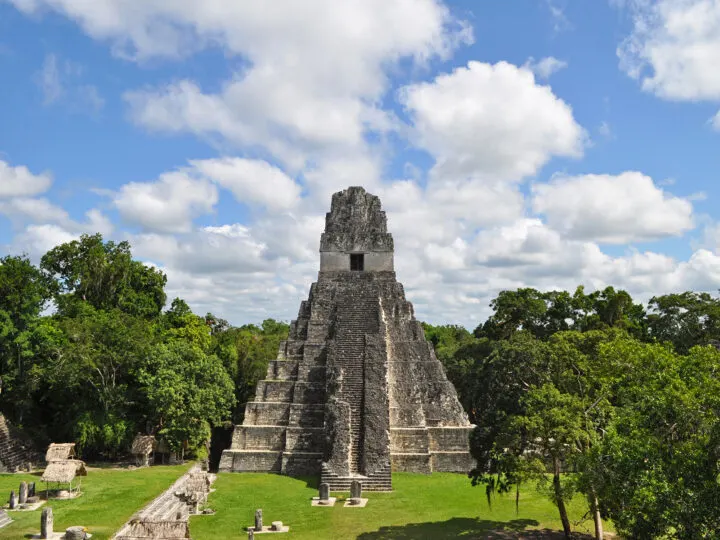 visiting Tikal seeing large temples of stone with trees on a blue sky day