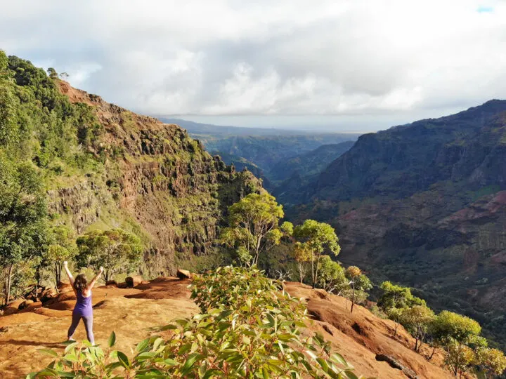hiking Waimea canyon trail picture of woman standing at entrance of canyon with lush greenery