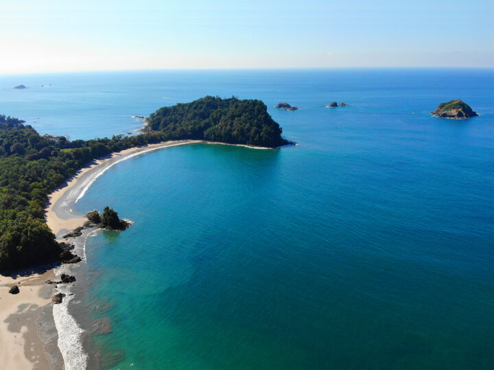 best beaches in Manuel Antonio teal water bright tan beach crescent shape with green trees
