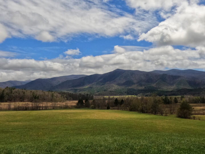 cades cove view of smoky mountains beyond field and blue sky with white clouds
