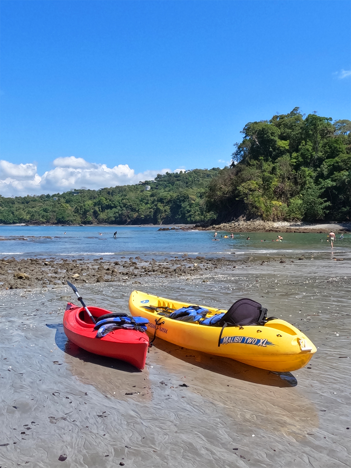 red and yellow kayaks on beaches of Manuel Antonio with rocky shoreline blue skies and trees