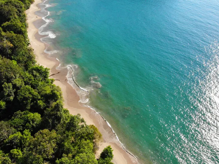 best beaches in Manuel Antonio picture from above with beach, white waves, teal water and trees